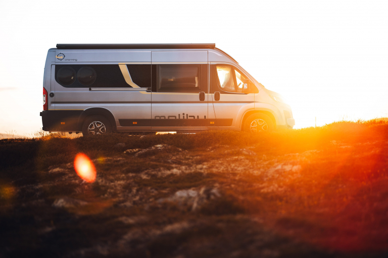 Seitenansicht eines Malibu Campervans bei Sonnenuntergang auf felsigem kahlem Untergrund.