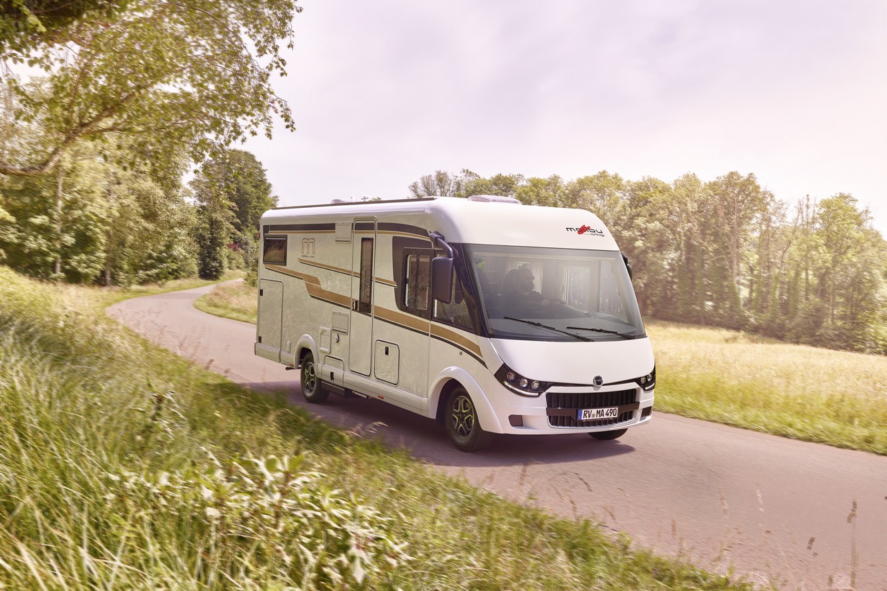 Malibu Reisemobil Fahrtbild auf der Straße, im Vordergrund und Hintergrund Wiese und Wald