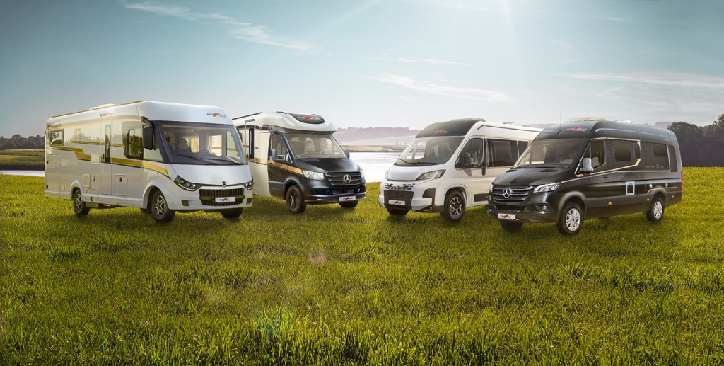 Zwei Malibu Reisemobile und zwei Malibu Campervans auf einer Wiese vor einem See.