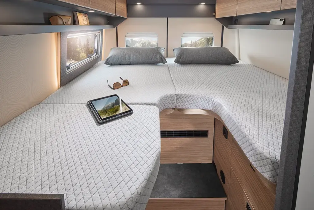 Espace nuit spacieux dans le camping-car Malibu relax, avec un matelas confortable, un espace de rangement et une vue sur l'extérieur grâce à trois baies