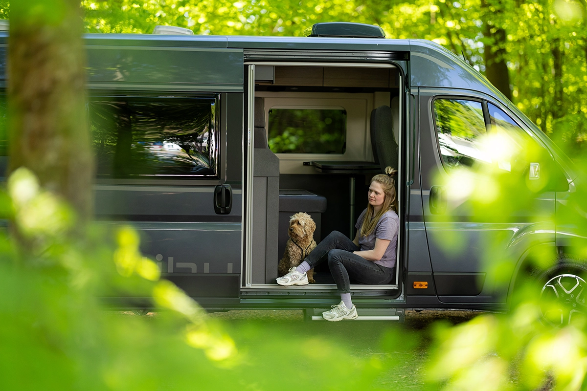 Malibu Relax Camper Van mit Frau und Hund im Wald – gemütlicher Einstiegsmoment für Reisen mit Haustier
