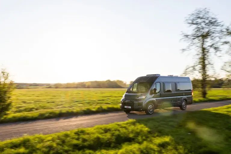 Malibu Camper Van fährt bei Sonnenuntergang durch grüne Landschaft auf einer Landstraße