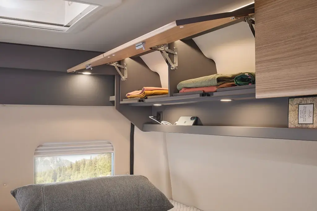Armoire supérieure ouverte dans le camping-car Malibu Relax, contenant des vêtements pliés et des compartiments de rangement