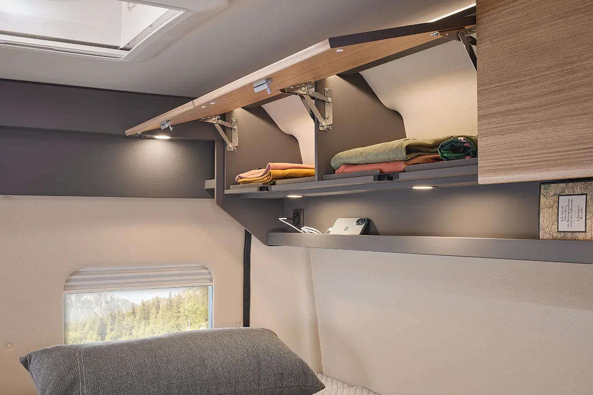 Offener Oberschrank im Malibu Relax Camper Van mit gefalteter Kleidung und Ablagefächern