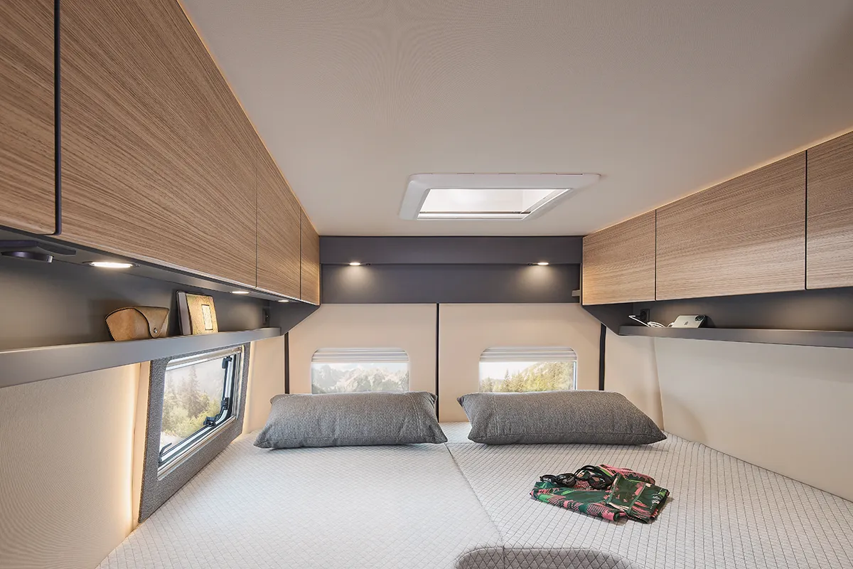Schlafbereich im Malibu Relax Camper Van mit Dachfenster, seitlichen Hängeschränken und gemütlicher Bettfläche