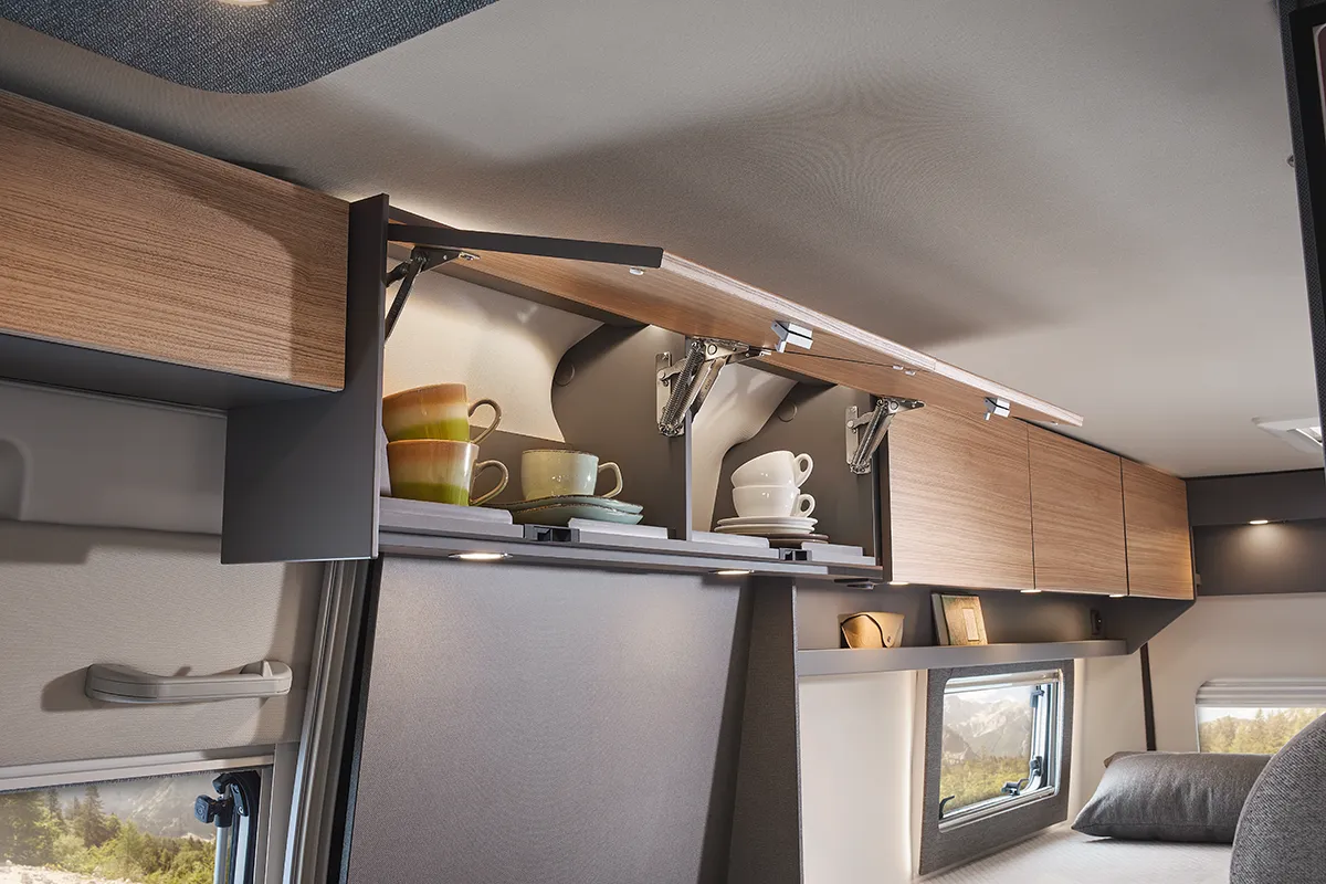 Offene Hängeschränke im Malibu Relax Camper Van mit sicher verstautem Geschirr und Tassen – intelligentes Stauraumdesign im Wohnbereich