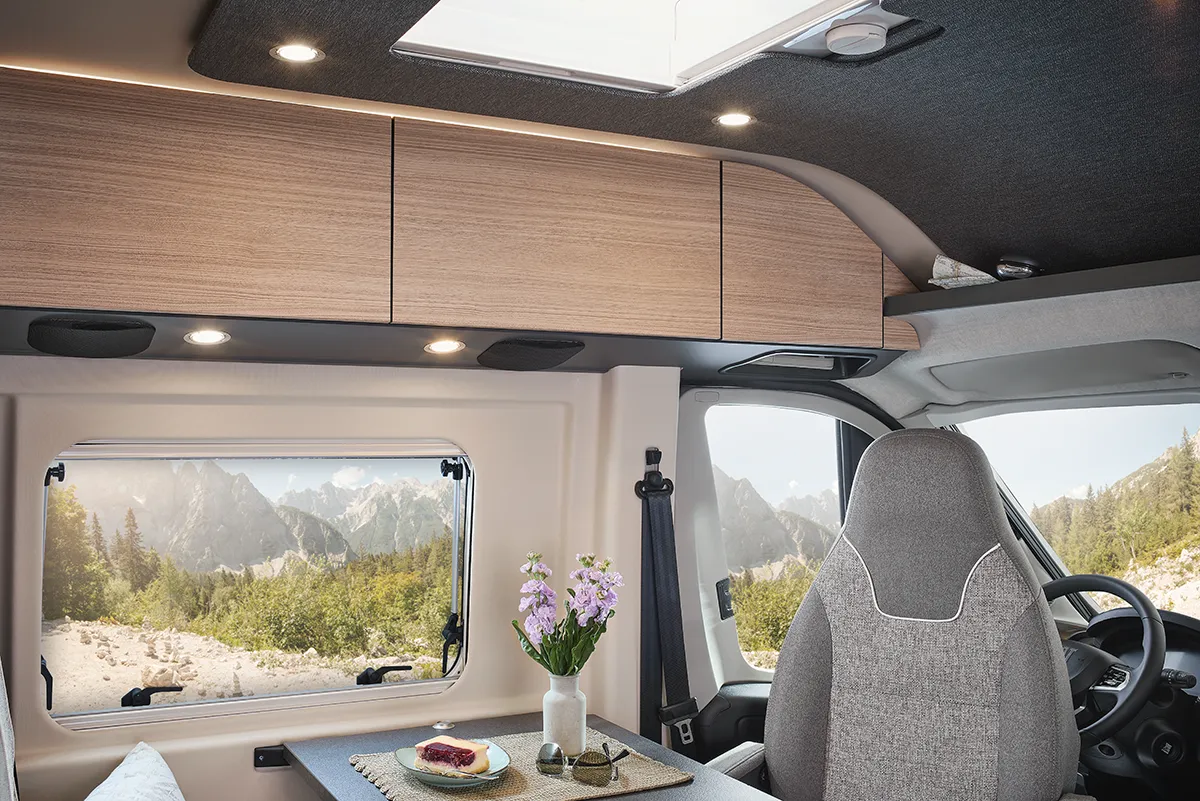 Malibu Relax Camper Van mit Panoramafenster, Dachluke und modernen Hängeschränken – Blick in den gemütlichen Essbereich mit Bergkulisse