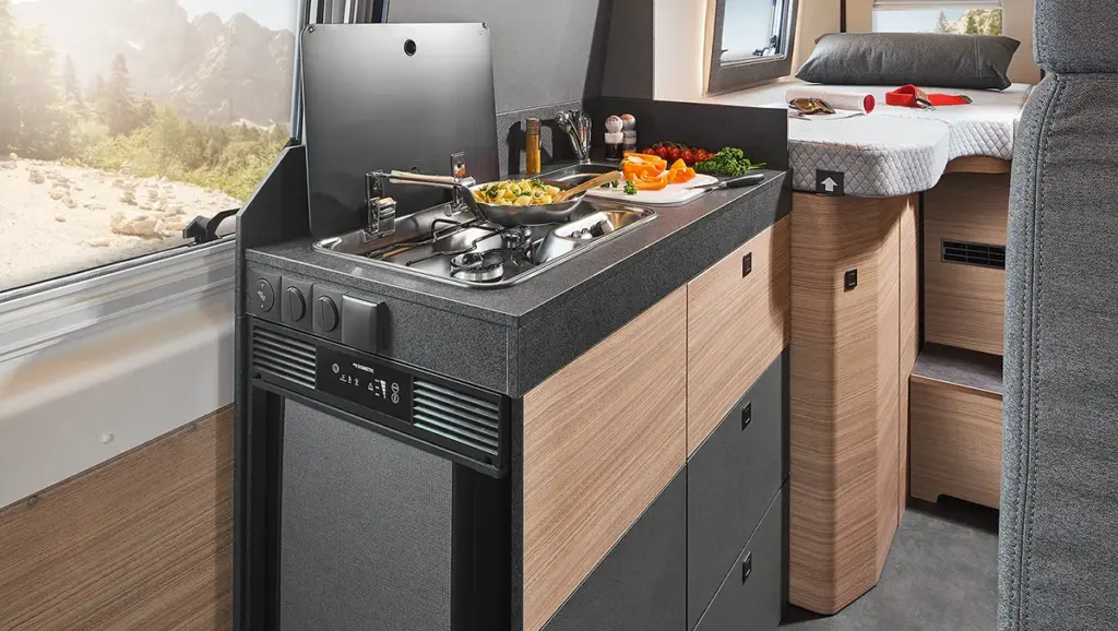 Cuisine intégrée dans le camping-car Malibu relax, avec table de cuisson à gaz, évier, réfrigérateur et ingrédients frais pour préparer des pâtes