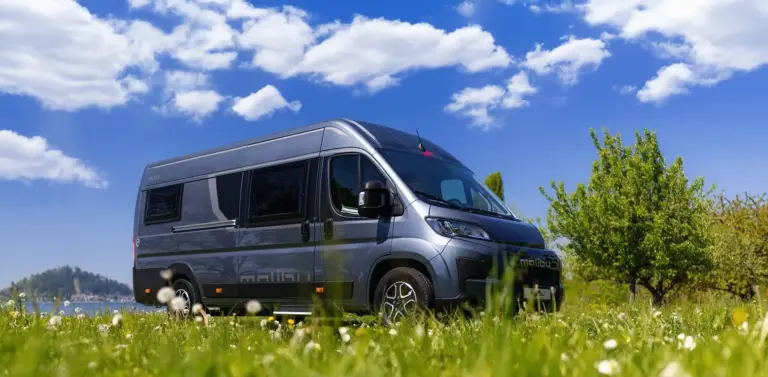 Malibu Relax Camper Van auf einer Frühlingswiese vor blauem Himmel