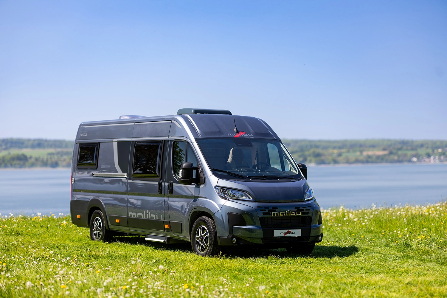 Malibu Relax Camper Van auf grüner Wiese mit Blick auf See und Hügellandschaft