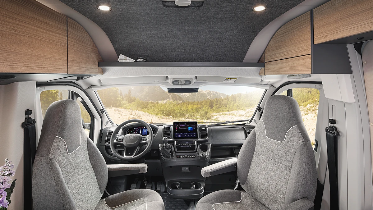 Innenansicht des Malibu Relax Camper Vans mit drehbaren Vordersitzen, modernem Cockpit und großzügigem Blick durch die Frontscheibe auf eine Berglandschaft – komfortables Fahrerlebnis mit Stil.