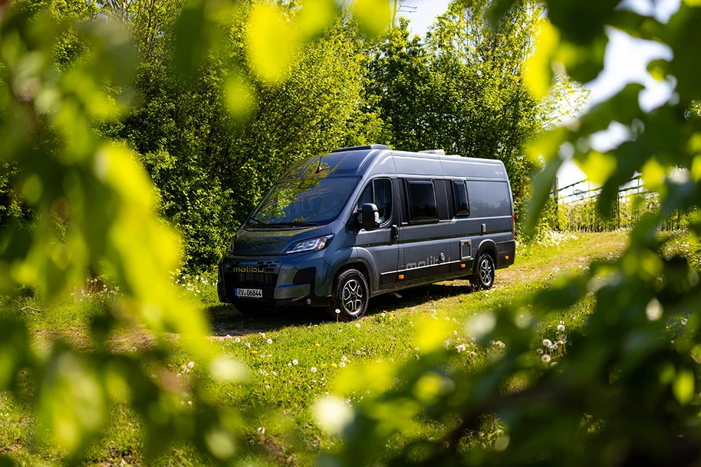 Malibu Relax Camper Van auf einem grünen Naturweg zwischen Bäumen