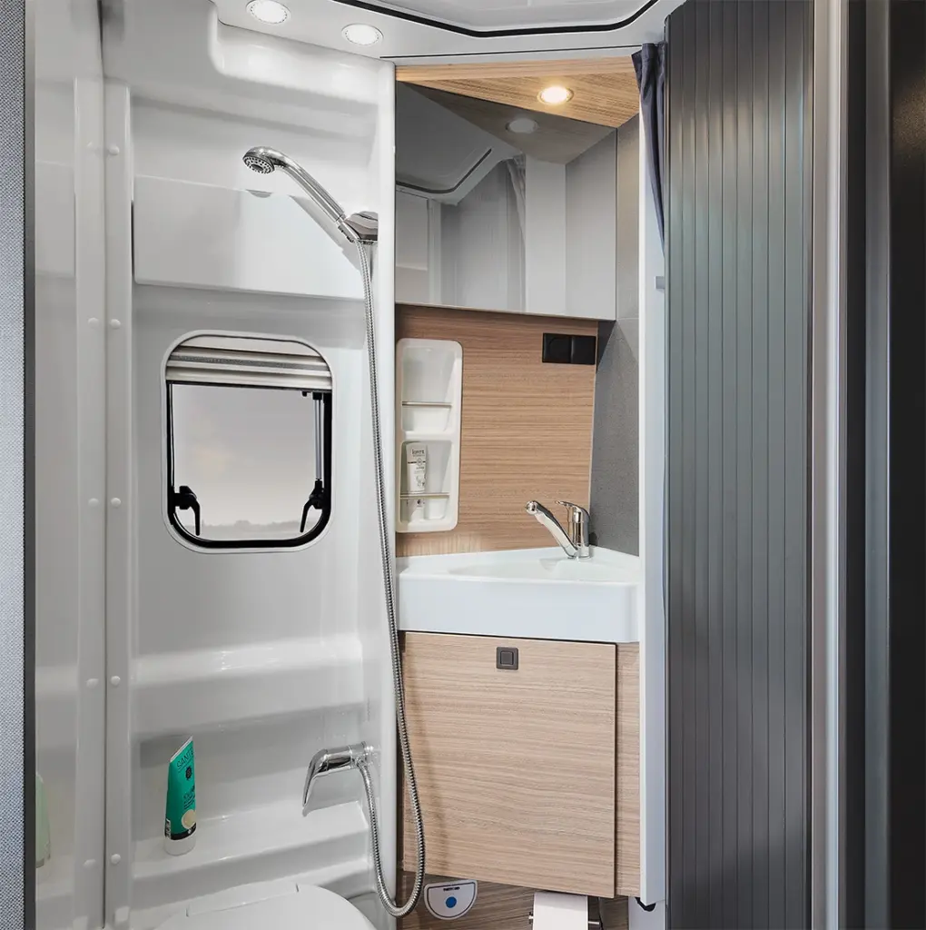 Salle de bains moderne dans le camping-car Malibu Relax, équipée d'un lavabo, d'une armoire de toilette, d'une douche et d'une fenêtre laissant entrer la lumière du jour, pour une sensation d'espace et de luminosité