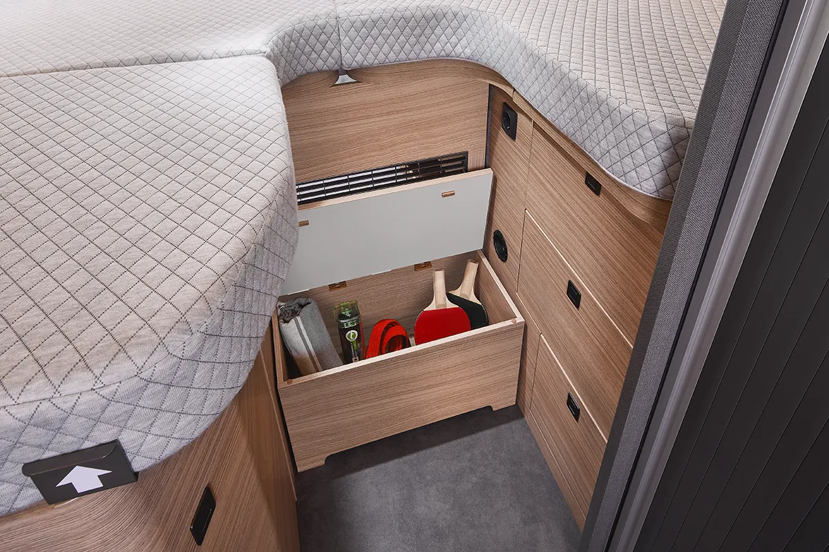 Geräumiger Stauraum in der Trittstufe des Malibu Relax Camper Vans mit geöffnetem Fach und Freizeitutensilien wie Tischtennisschlägern und Decke
