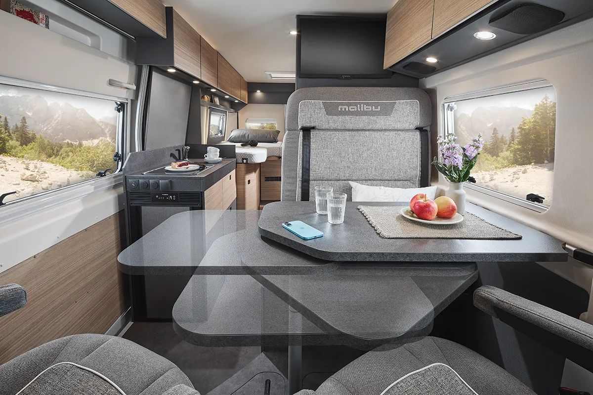 Gemütlicher Wohn- und Essbereich im Malibu Relax Camper Van mit hochwertiger Sitzgruppe, Klapptisch und moderner Küchenzeile vor alpiner Kulisse