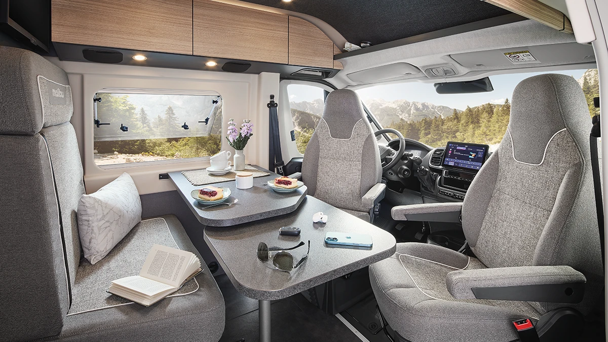 Heller Wohn- und Essbereich im Malibu Relax Camper Van mit gedecktem Frühstückstisch, ergonomischen Sitzen, großem Seitenfenster mit Panoramablick auf die Berge