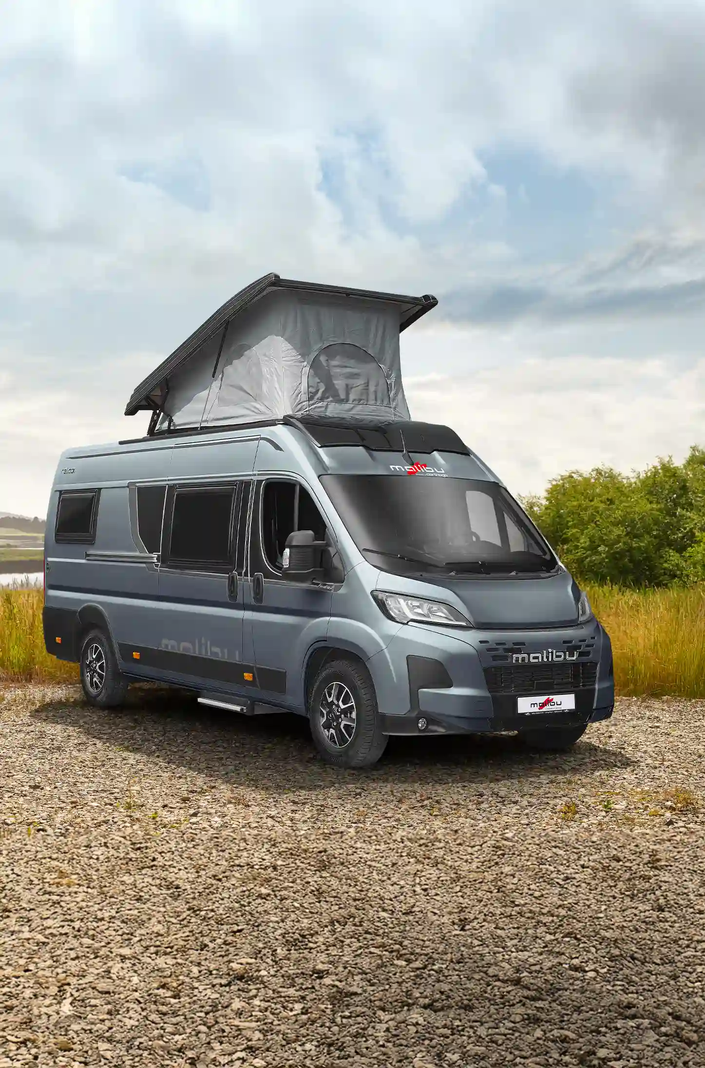 Relax Camper Van mit Aufstelldach auf freier Wiese vor bewaldeter Naturkulisse