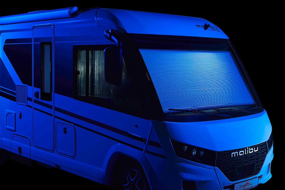 Ein modernes Malibu-Wohnmobil wird in blauer Beleuchtung gezeigt, wobei die Seitenfenster und die große Frontscheibe durch reflektierende Jalousien vor einem schwarzen Hintergrund abgedeckt sind.