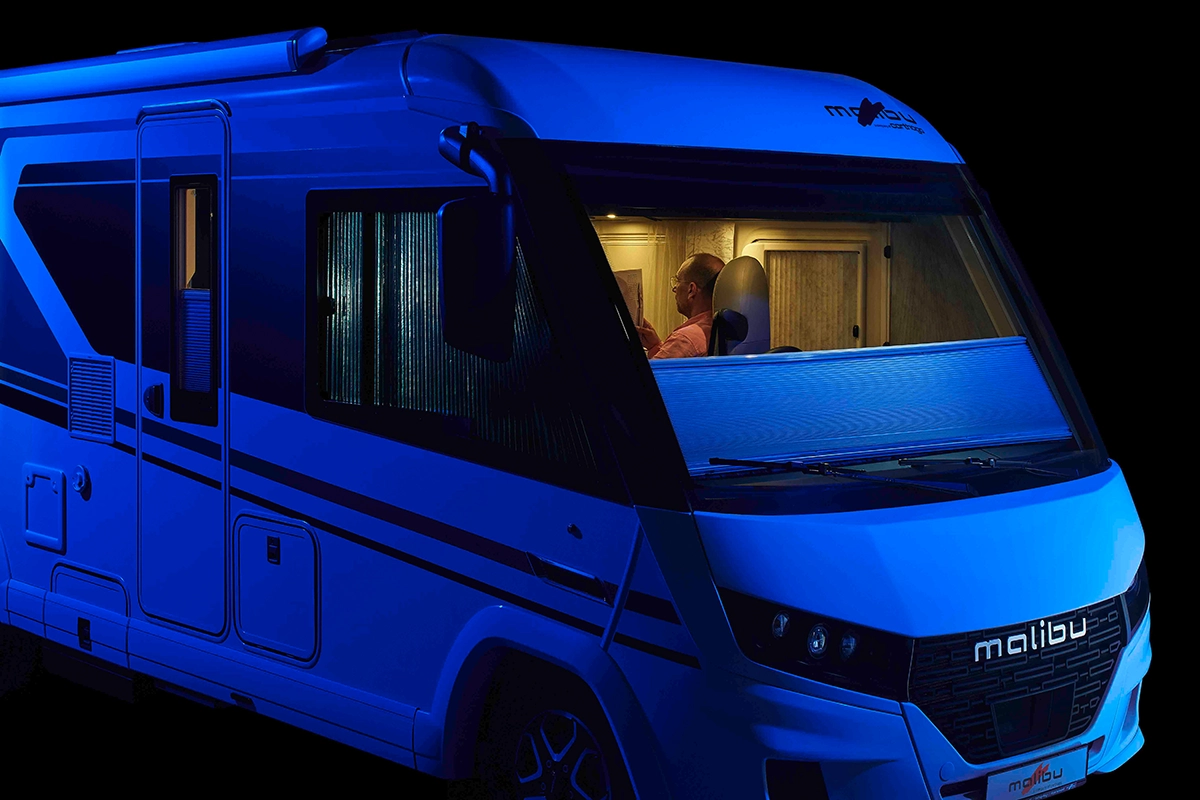 Ein Mann sitzt nachts in einem Wohnmobil in Malibu, das mit blauem Licht beleuchtet wird und dessen Fenster zum Schutz der Privatsphäre zugezogen sind.