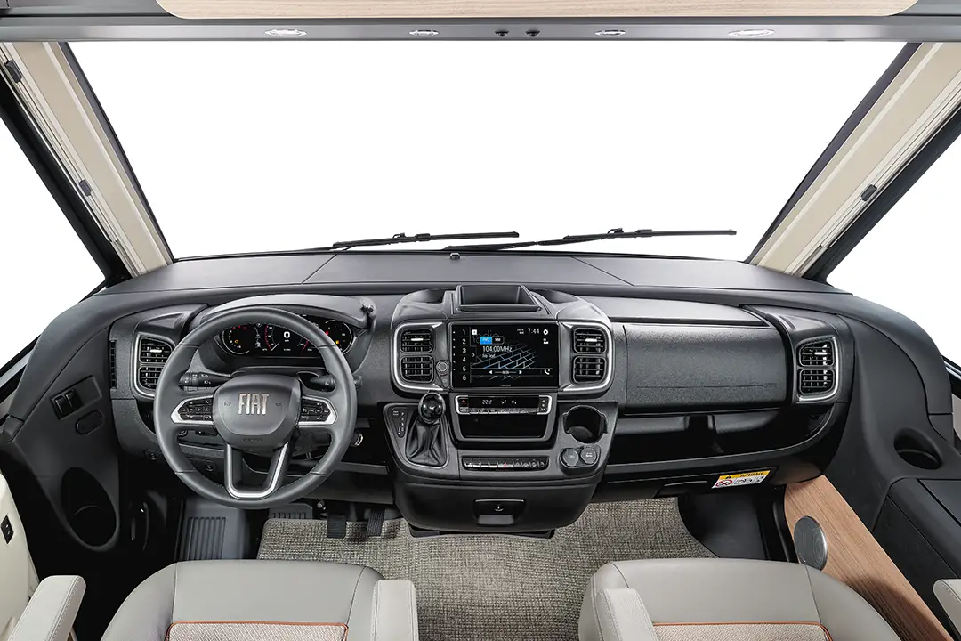 Blick auf ein modernes Wohnmobil-Cockpit mit Fiat-Lenkrad, Bedienfeld, großem Touchscreen-Display und beigen Ledersitzen. Das Armaturenbrett und die Fenster bieten einen Panoramablick nach vorne.