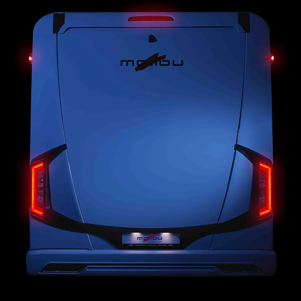 Die Rückansicht eines blauen Malibu bei Nacht, mit beleuchteten roten Rückleuchten, einer zentralen Bremsleuchte und dem Malibu-Logo über dem Nummernschild.