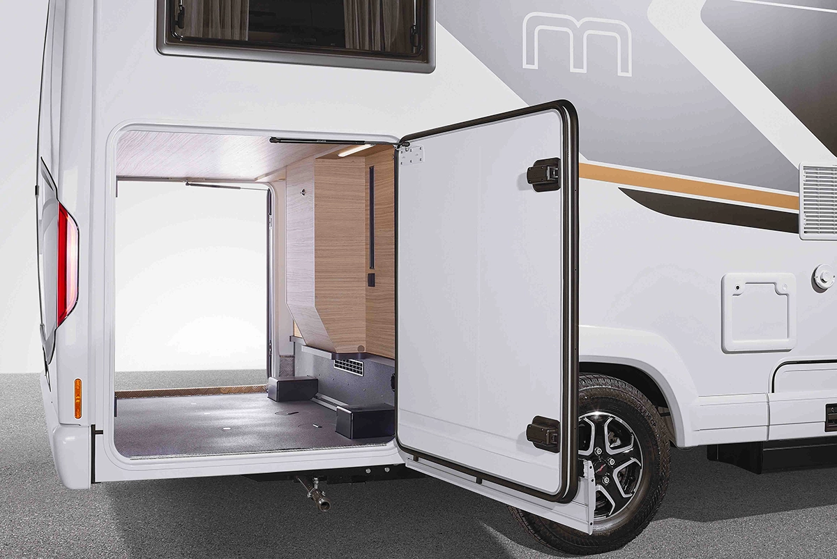 Eine Nahaufnahme des offenen hinteren Stauraums eines Wohnmobils, die einen geräumigen, holzgetäfelten Innenraum mit geöffneter Seitentür und einem Teil eines Rades und der Außengestaltung zeigt.