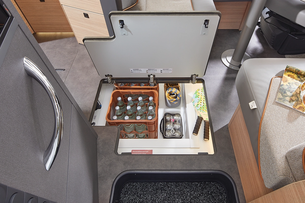 Ein offenes Bodenfach in einem Wohnmobil bietet Stauraum für Wasserflaschen, Glasflaschen, Snacks und andere Dinge, die in Fächern unter dem Sitzbereich geordnet sind.