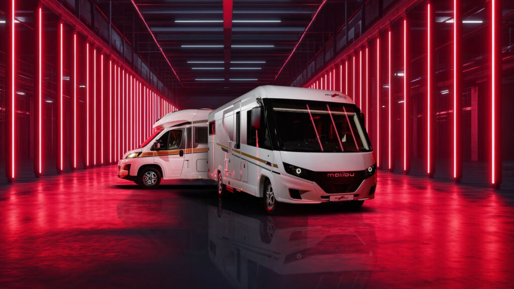 Twee moderne witte campers staan binnen geparkeerd, omringd door heldere verticale rode lampen die weerkaatsen op de glimmende vloer, wat een futuristische sfeer creëert.