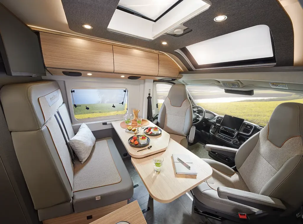 Fahrerhaus Malibu Van first - two rooms, die Fahrersitze sind nach innen gedreht, es entsteht eine Sitzgruppe um einen Tisch.